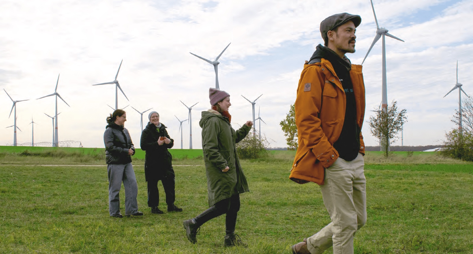 Mitarbeitende von co2online laufen über eine grüne Wiese, im Hintergrund steht ein gutes Dutzend Windräder