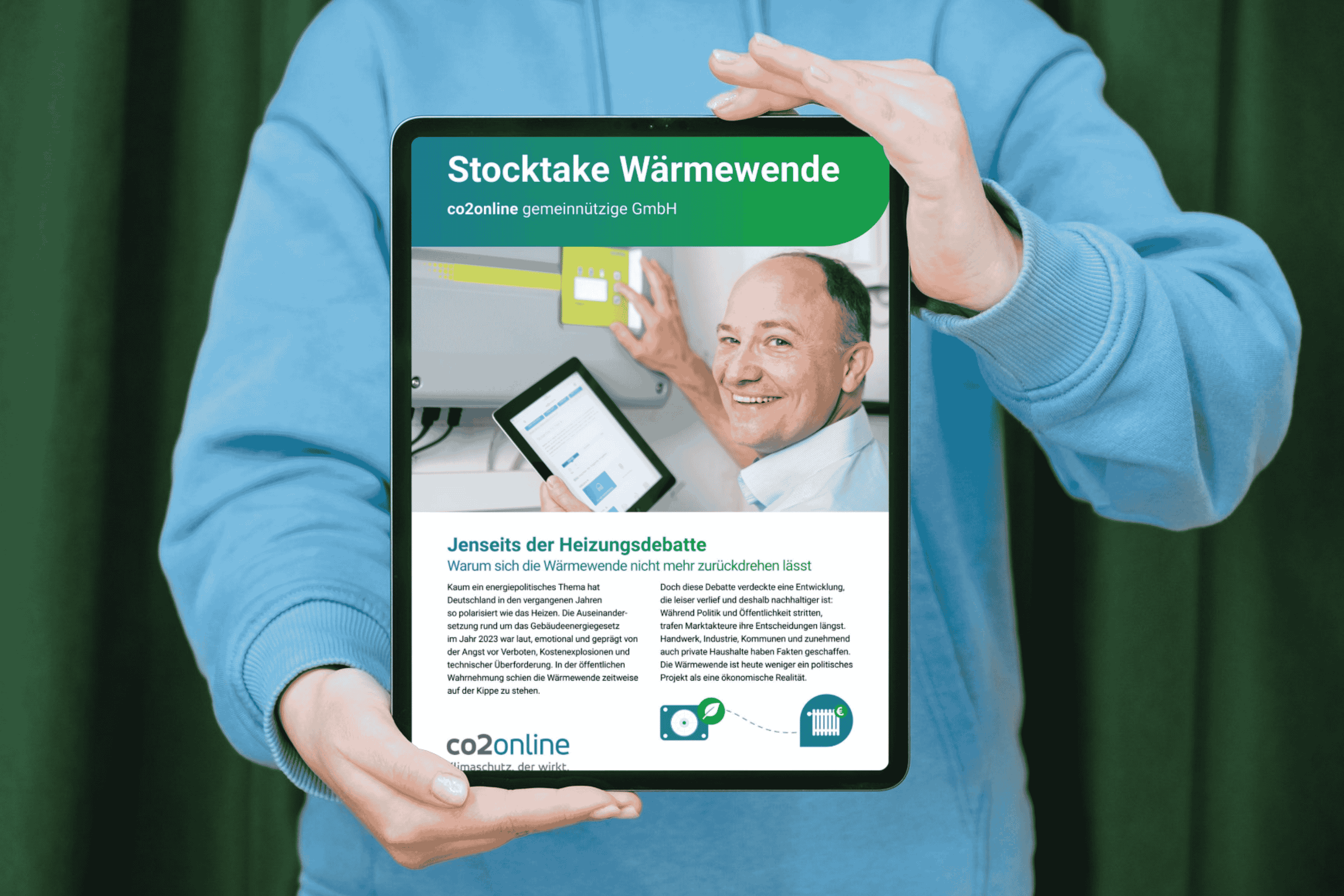 Person mit blauem Pullover hält vor sich ein Tablet mit der Publikation "Stocktake Wärmewende".