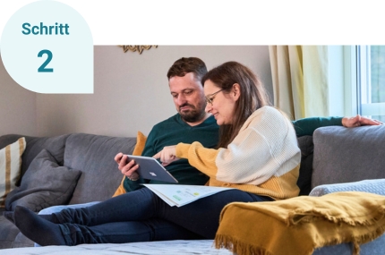 Schritt 2: Die beiden Einfamilienhausbesitzer zu Hause auf ihrem Sofa schauen sich das HeizCheck-Ergebnis auf dem Tablet an.