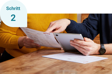 Eine Person hält eine Abrechnung in der Hand, die andere übertragt die Daten in den ModernisierungsCheck auf dem Tablet.
