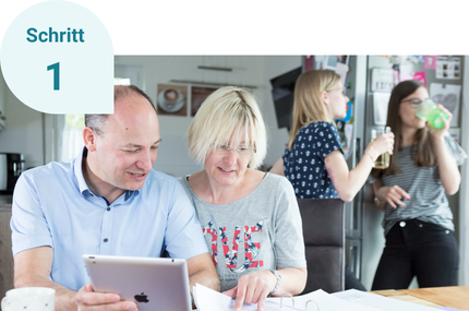 Schritt 1: Zwei Personen durchlaufen den WärmepumpenCheck am Tablet. Im Hintergrund stehen zwei junge Frauen.