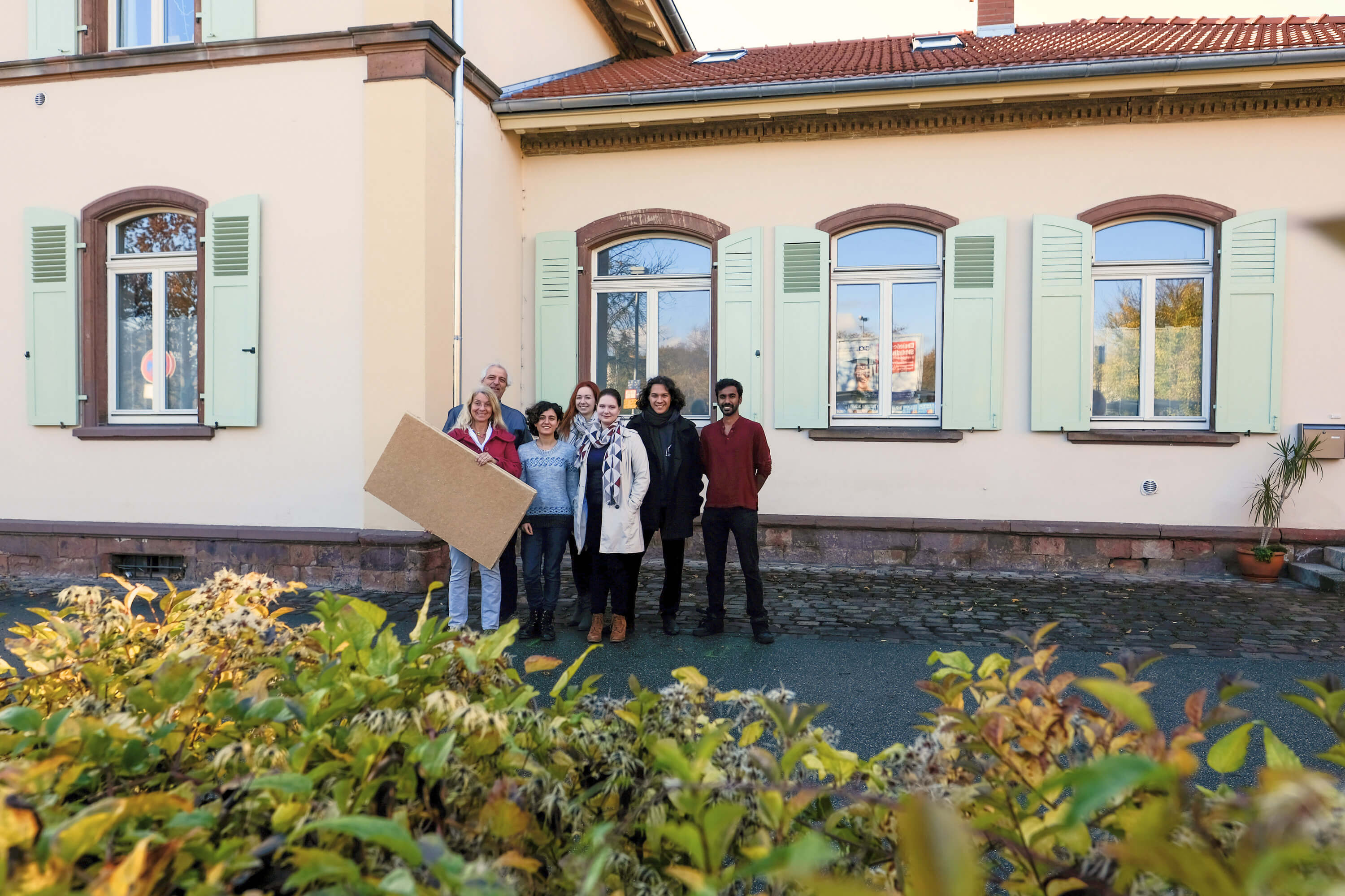 Mehrere Personen stehen vor einem Haus. Sie haben eine große Dämmplatte in der Hand. 