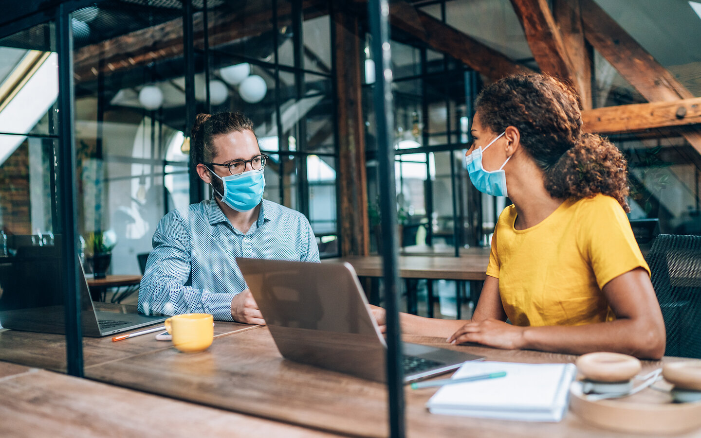 Zwei Personen mit Masken sprechen in einem modernen Büro.