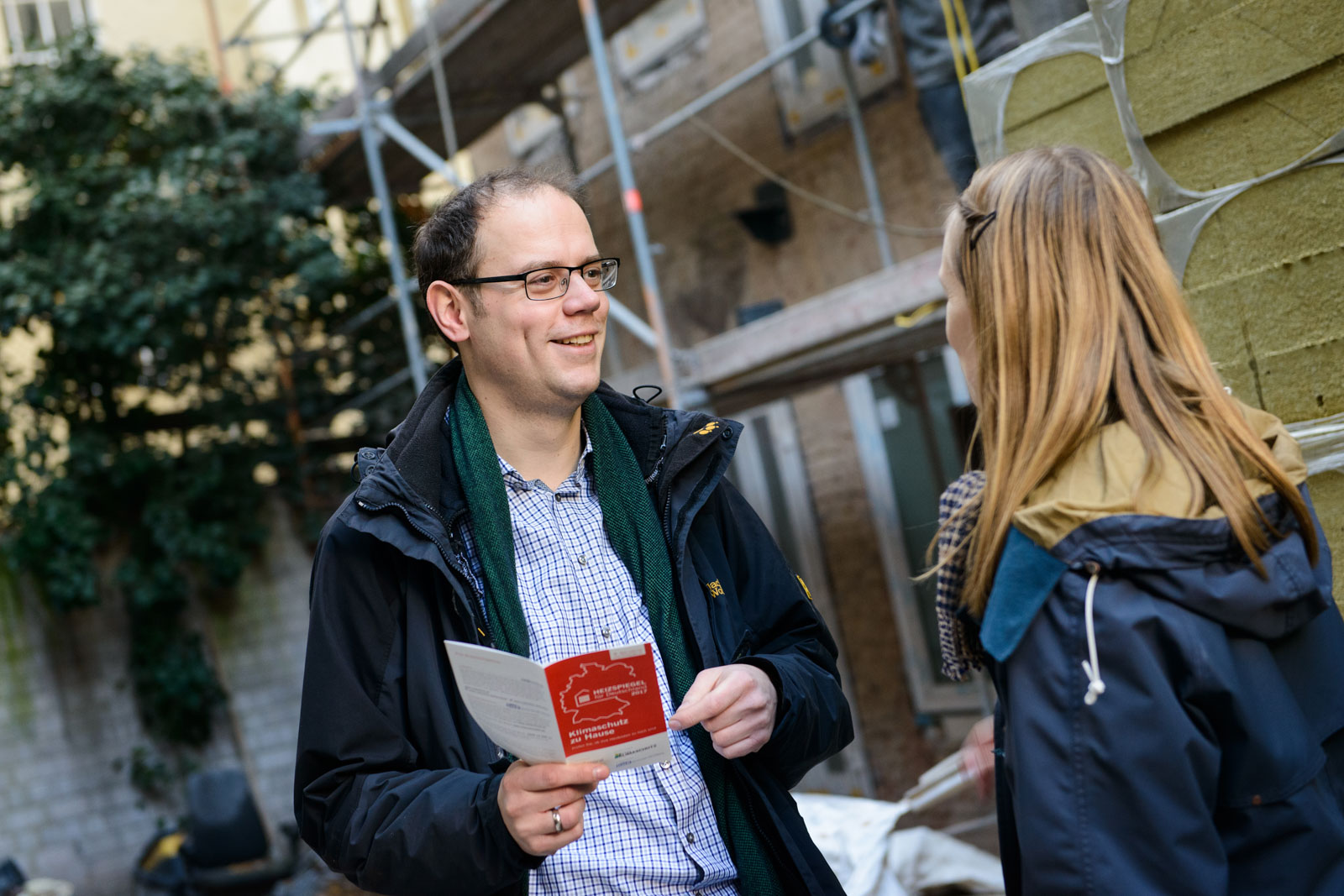 Till Eichmann vor einem Gebäude im Gespräch mit einer Frau. Er hält einen Heizspiegel-Flyer in der Hand. 