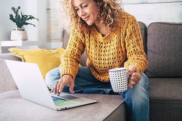 Frau sitzt am Notebook auf dem Sofa zu Hause