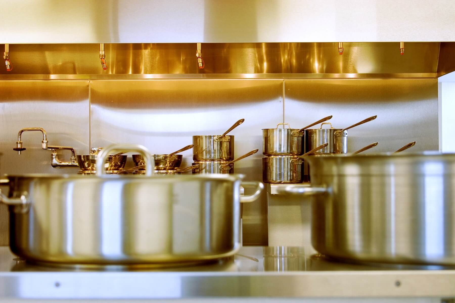 Silberne Töpfe mit Deckel auf Herd mit weiteren Töpfen im Hintergrund