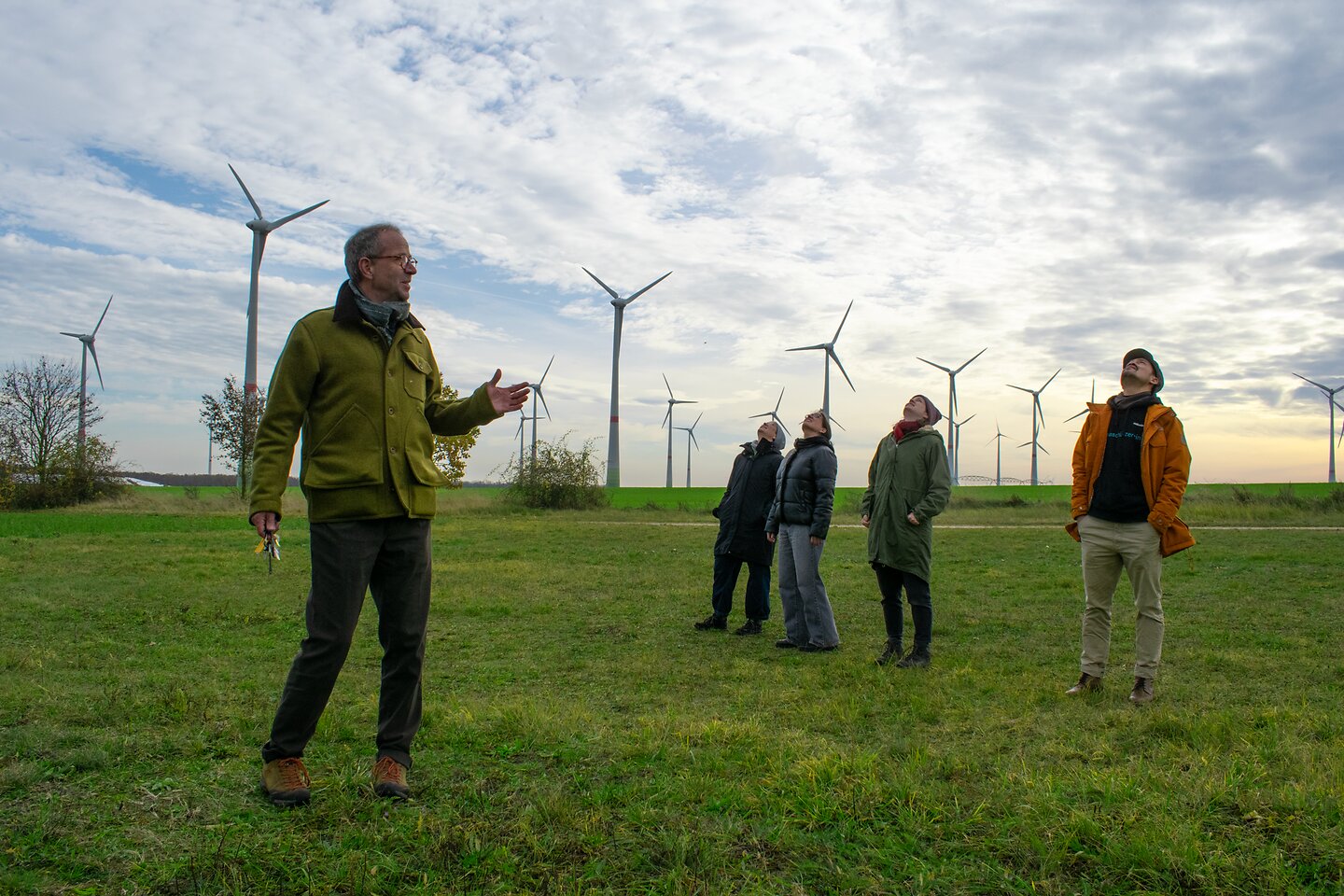 Fünf Menschen auf dem Feld schauen auf Windräder im energieautarken Dorf Feldheim.