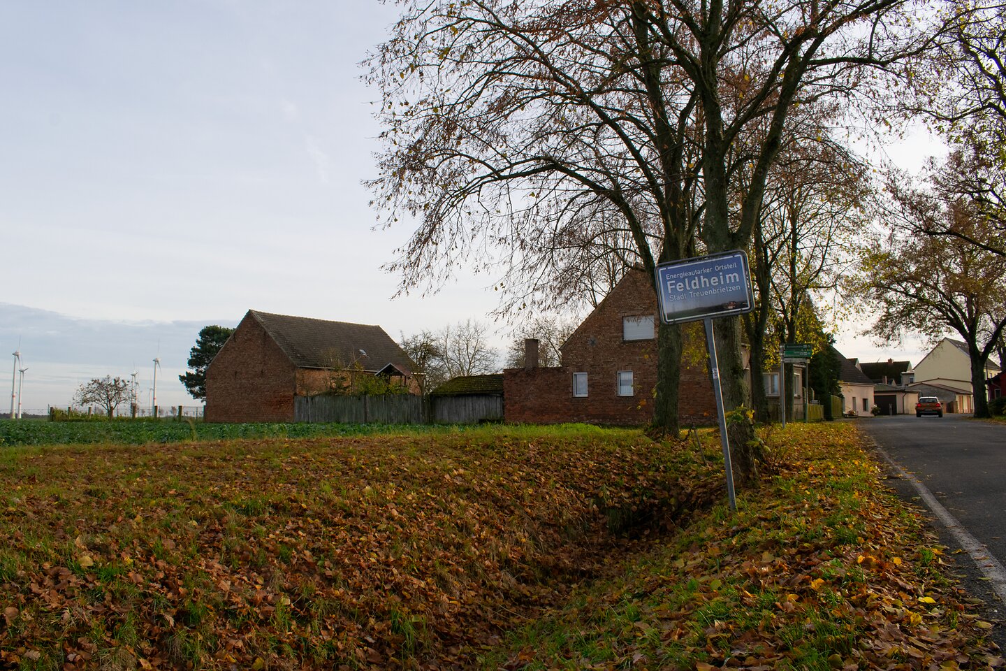 Ortsschild Feldheim und dahinter die ersten Häuser des Dorfes.