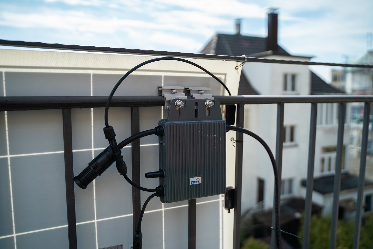 Im Vordergrung ein Detail einer Balkon-PV-Anlage, dahinter ist eine Stadt zu sehen.