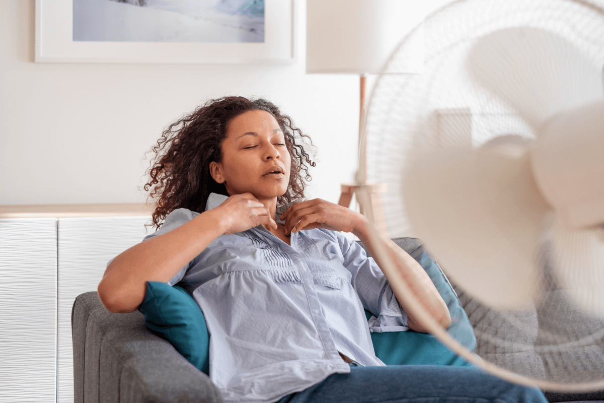 Eine Frau sitzt vor einem laufenden Ventilator.