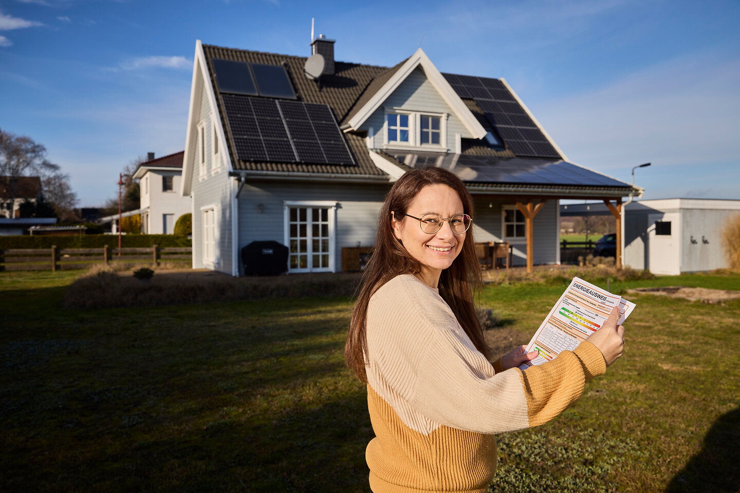 Eine Frau vor dem Haus mit einem Energieausweis in der Hand.