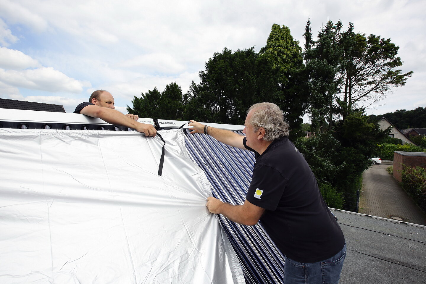 Zwei Handwerker montieren Solarthermieanlagen auf einem Dach. 
