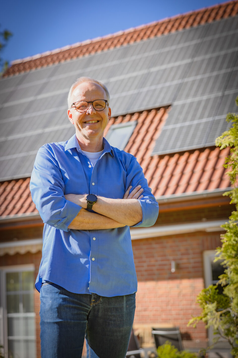 Praxistester Kai steht glücklich vor seinem Haus mit Photovoltaikanlagen auf dem Dach.