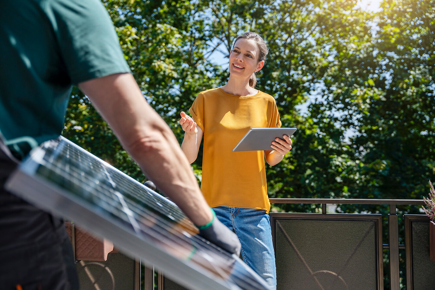 Handwerker hält ein Solarpanel unter dem Arm und wird von einer Frau angesprochen