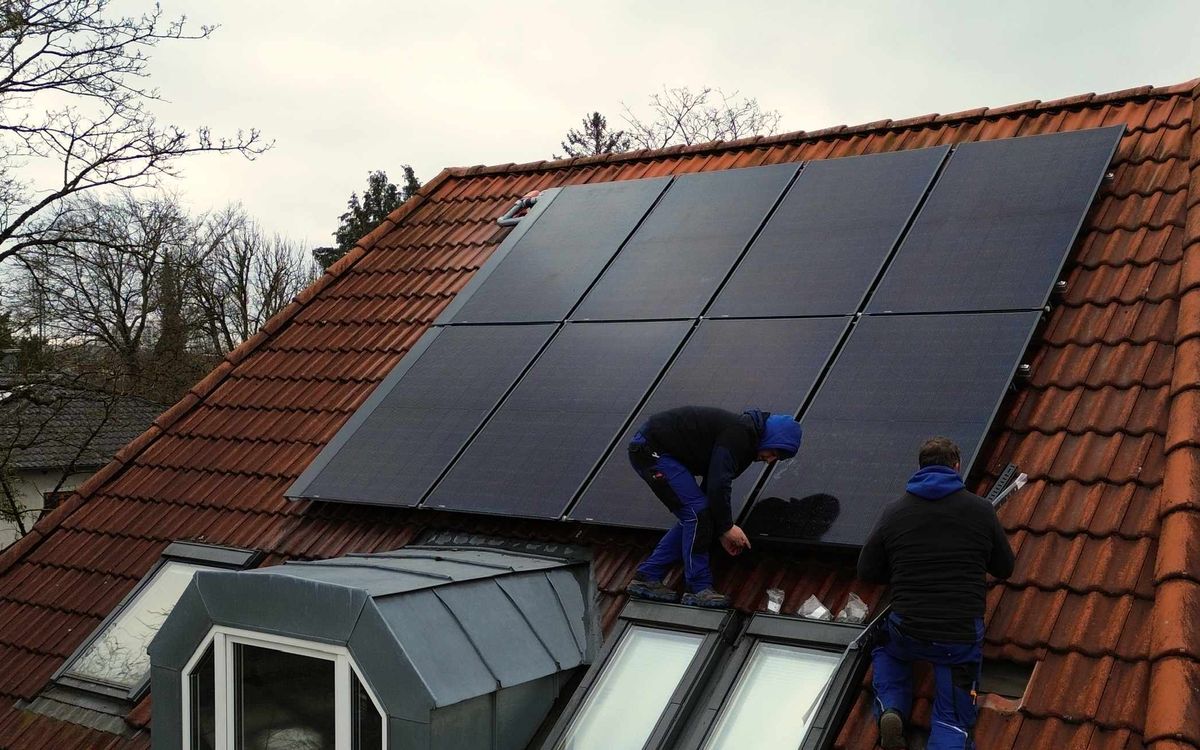 Zwei Handwerker montieren PVT-Kollektoren auf einem Altbau-Dach.