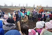 Baumpflanz-Aktion des MIYA e. V.: Menschen (vor allem Kinder) stehen im Kreis um einen Mann, der einen Baum pflanzt