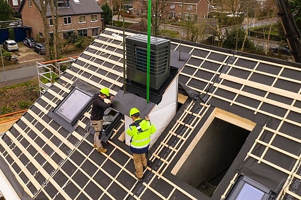 Serielle Sanierung: Haustechnik-Modul beim Einbau (Bauarbeiter auf Hausdach mit Öffnung, Haustechnik-Modul an Kran-Seilen).