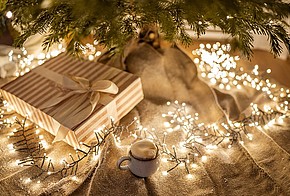Lichterkette, Weihnachtsbaum, Geschenk und ein Heißgetränk.