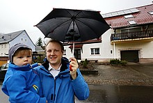 Praxistest-Teilnehmer Carsten Tamm mit Sohn und Regenschirm vor seinem Haus mit Solarthermieanlage