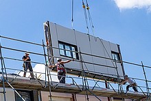 Energiesprong: serielle Sanierung in Longueau/Frankreich (Baugerüst mit Bauarbeitern und Fassadenelement an Kran-Ketten).
