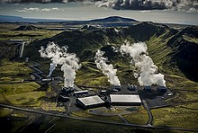 Hellisheidi Power Plant in Island: Luftaufnahme der Industrieanlage mit viel Wasserdampf, umgeben von Grün und Bergen.