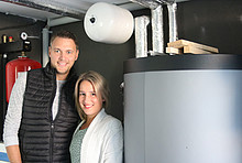 Stefan und Stefanie Breit im Heizungskeller, rechts neben ihnen der graue Warmwasserspeicher