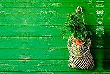 Grüne Holzwand, rechts ein Stoffbeutel mit Gemüse