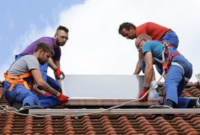Installation Solarthermie: Männer heben einen Kollektor aufs Dach