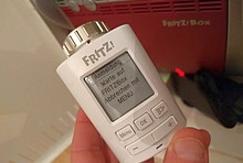Smartes, weißes Thermostat in der Hand vor rotem Router: AVM Fritz!DECT 301 und AVM FritzBox