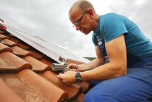 Mann auf Dach schließt Solarkollektor an