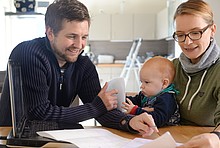 Familie Krämer aus Herford: Mann, Baby und Frau mit Laptop und Unterlagen zur Lüftung am Küchentisch