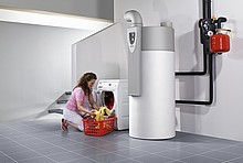 rechts eine große Warmwasser-Wärmepumpe, links kniet eine Frau vor Waschmaschine und Wäschekorb