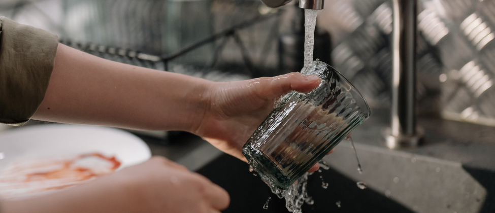 Person reinigt Wasserglas unter fließendem Wasserhahn 